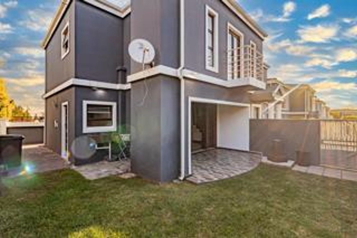 Rear view of a modern double-story house featuring a covered patio, small balcony, paved garden area, and secure boundary walling.