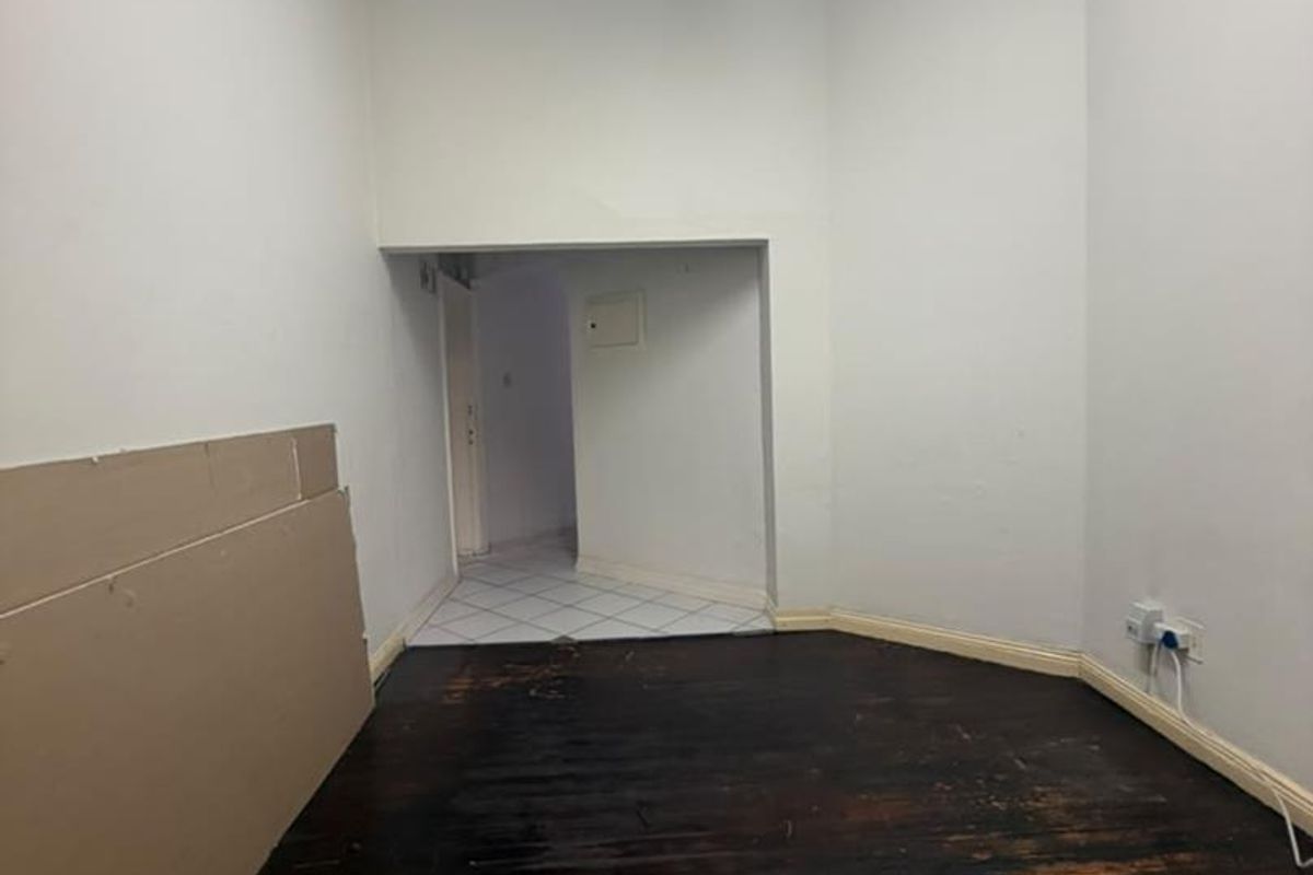 An empty room featuring worn hardwood flooring and plain white walls, offering a blank canvas for renovation and interior design updates.