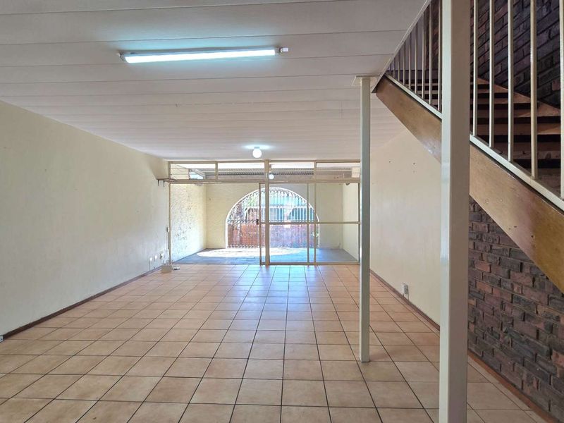 Spacious, empty living area featuring ceramic tile flooring, an exposed brick feature wall, and a staircase leading to the upper level.