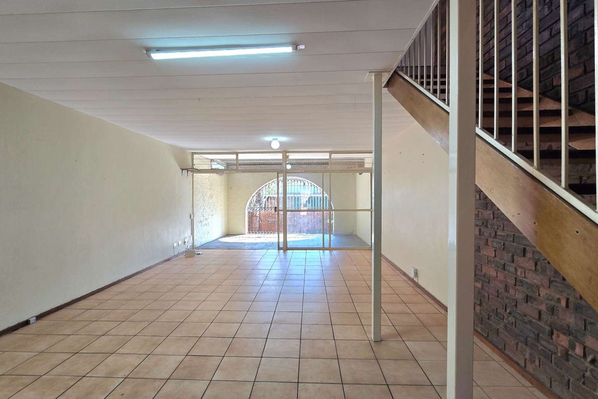 Spacious, empty living area featuring ceramic tile flooring, an exposed brick feature wall, and a staircase leading to the upper level.