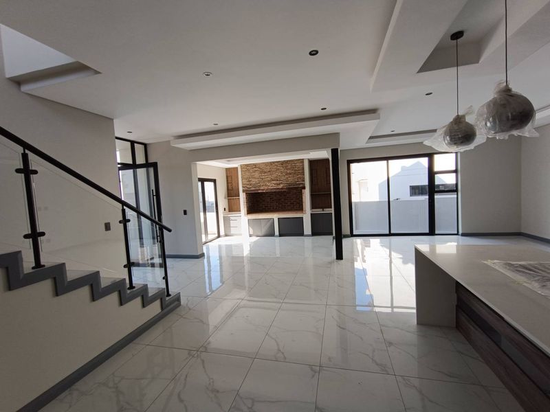 Spacious open-plan living area featuring modern porcelain tiling, a built-in fireplace with stone cladding, and a contemporary staircase with glass balustrades.