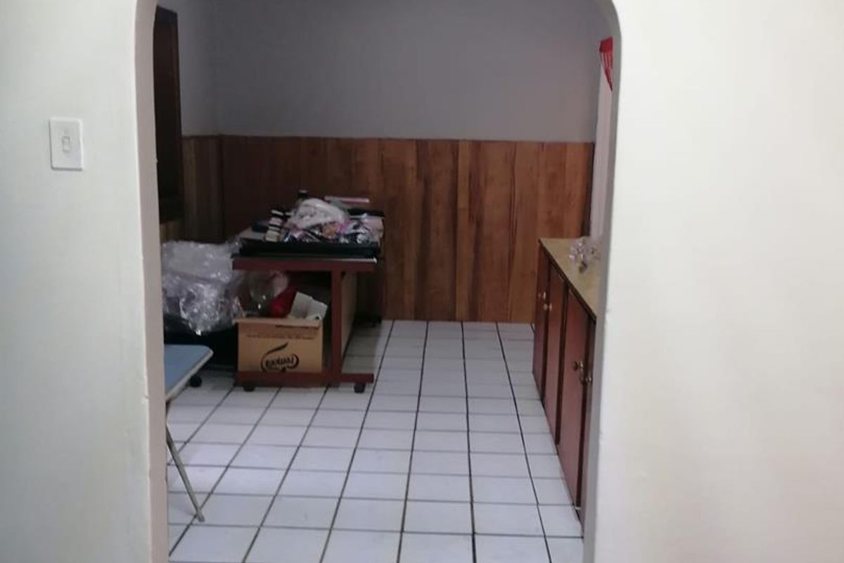 A view through an arched doorway into a kitchen area featuring tiled flooring, wooden wall paneling, and built-in cabinetry.