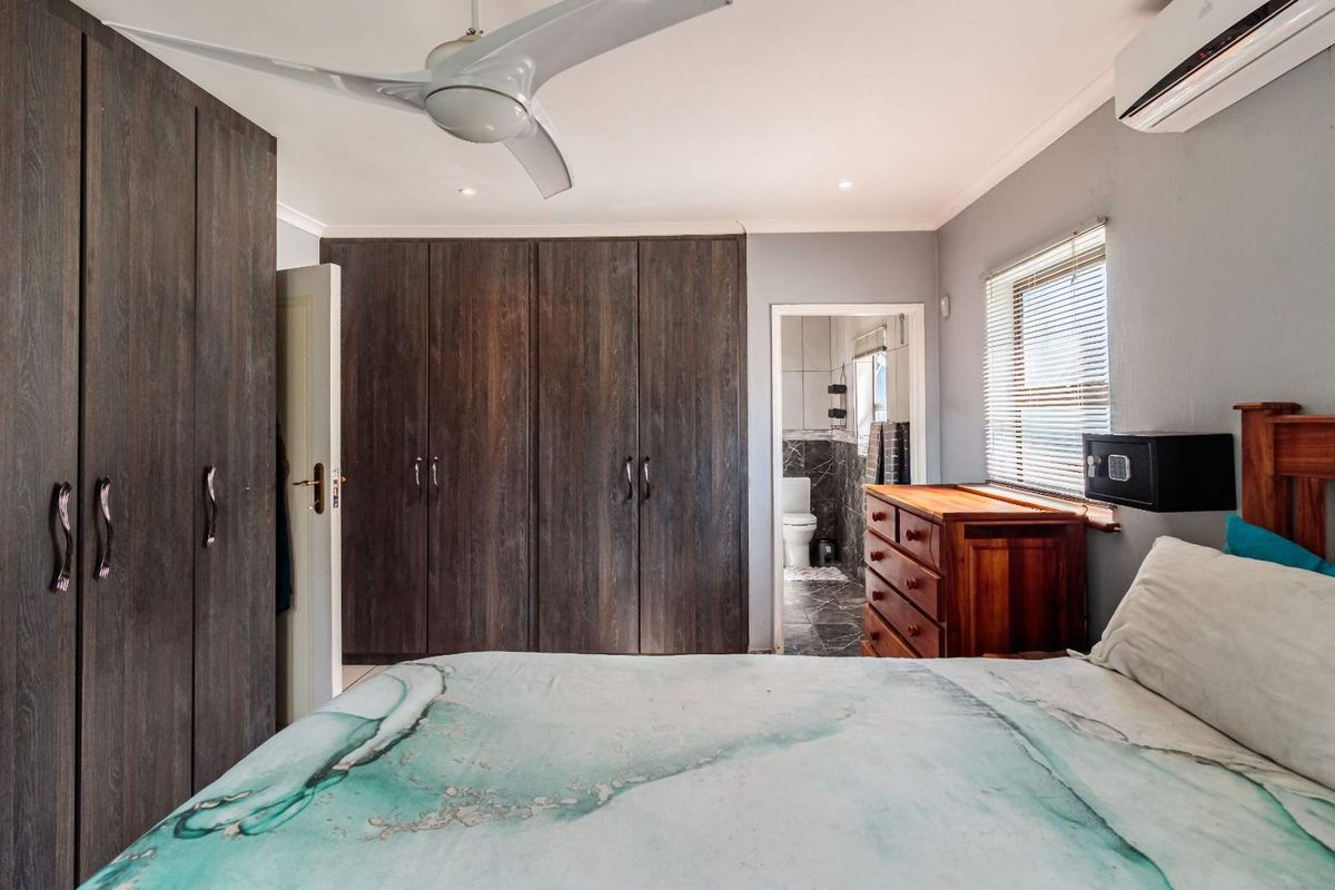 A well-maintained bedroom featuring built-in dark wood cabinetry, a ceiling fan, wall-mounted air conditioning unit, and an en-suite bathroom.
