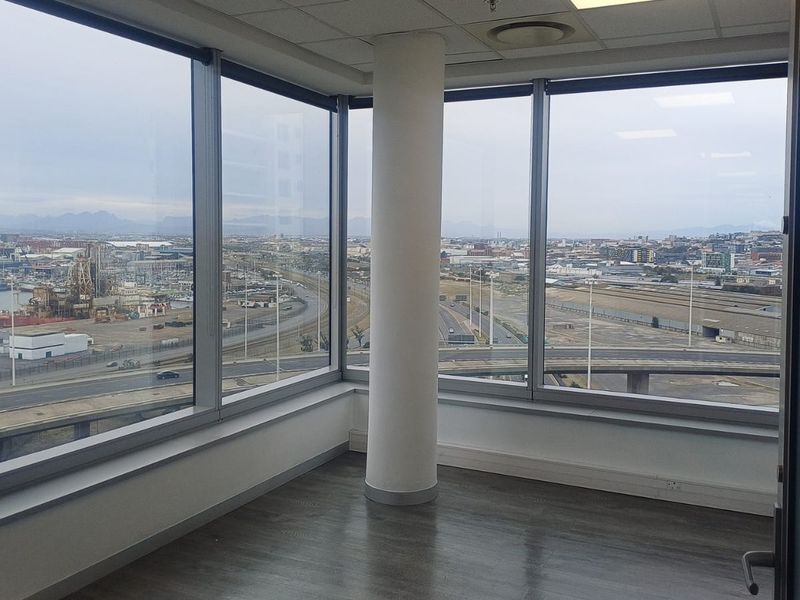 A bright, empty corner office space featuring expansive floor-to-ceiling windows with panoramic city and harbour views, laminate flooring, and a central structural column.