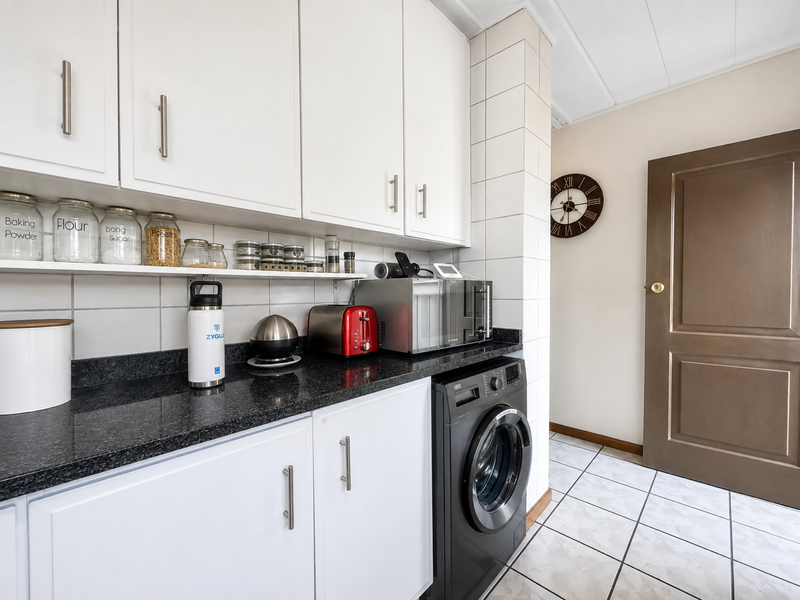 A functional scullery featuring white cabinetry, black granite countertops, tiled splashbacks, and a built-in washing machine, providing efficient utility space.