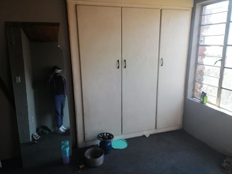 A bedroom featuring a built-in wardrobe and steel-framed window, requiring cosmetic updates to the flooring and wall finishes.
