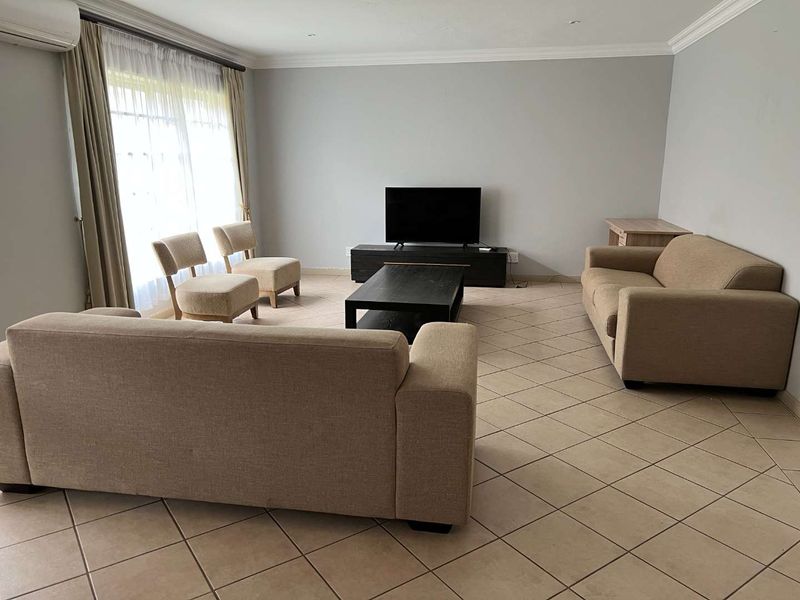 Spacious living room featuring neutral tiled flooring, recessed lighting, and a wall-mounted air conditioning unit, providing a comfortable and functional living space.