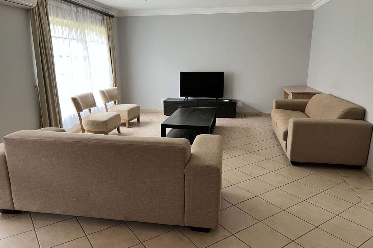 Spacious living room featuring neutral tiled flooring, recessed lighting, and a wall-mounted air conditioning unit, providing a comfortable and functional living space.