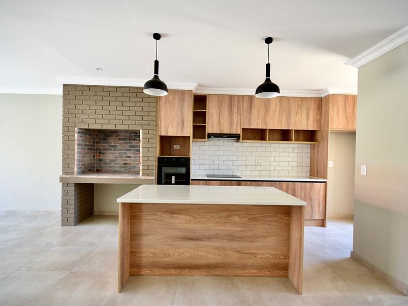 Modern open-plan kitchen featuring wood-look cabinetry, stone countertops, subway tile backsplash, built-in oven, and a unique integrated brick braai fireplace.