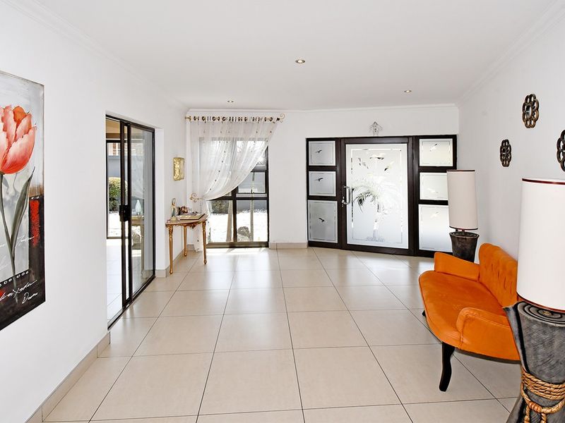 Spacious entrance hall featuring large format floor tiles, recessed lighting, and a decorative glass front door leading to the main living area.