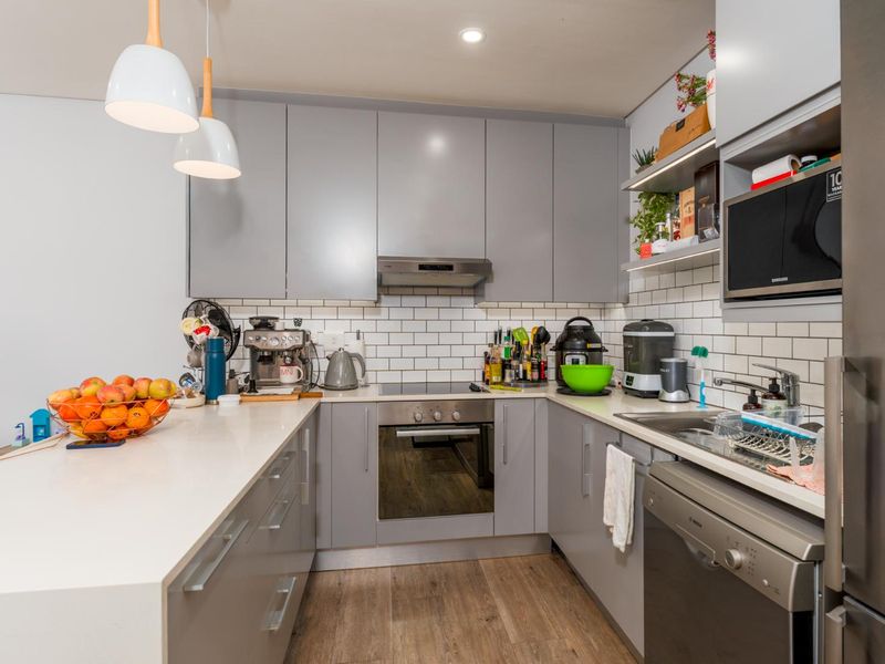 Modern kitchen featuring grey cabinetry, white stone countertops, subway tile backsplash, and integrated appliances including an oven, cooktop, and microwave.