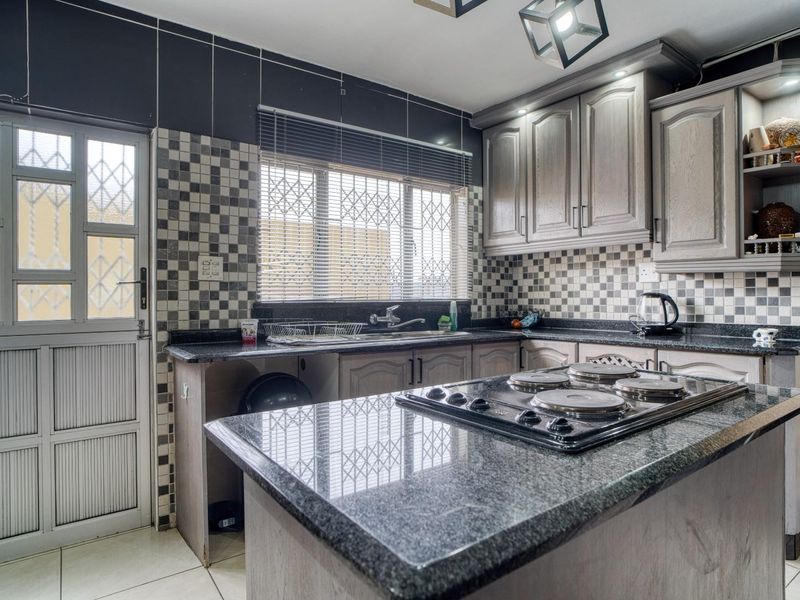 A functional kitchen featuring granite countertops, built-in cabinetry, a built-in hob, and a tiled backsplash with direct access to the exterior.