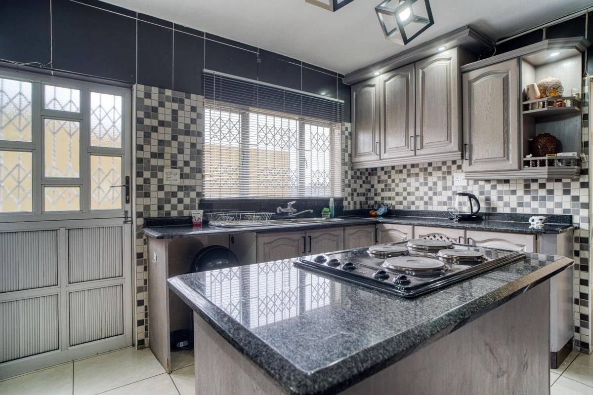 A functional kitchen featuring granite countertops, built-in cabinetry, a built-in hob, and a tiled backsplash with direct access to the exterior.