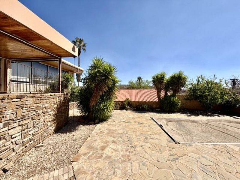 Outdoor pool area featuring stone paving, a covered patio with timber ceiling, and natural stone wall cladding.