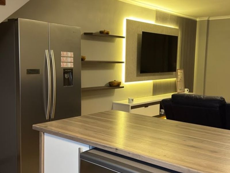 An open-plan living area featuring a modern kitchen island, built-in shelving with accent lighting, and a staircase leading to the upper level.