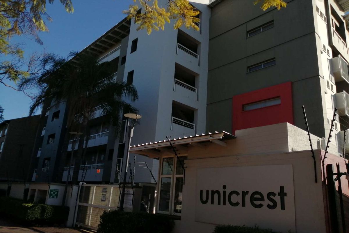 Exterior view of the Unicrest apartment complex featuring multi-story residential units with balconies and secure perimeter fencing.