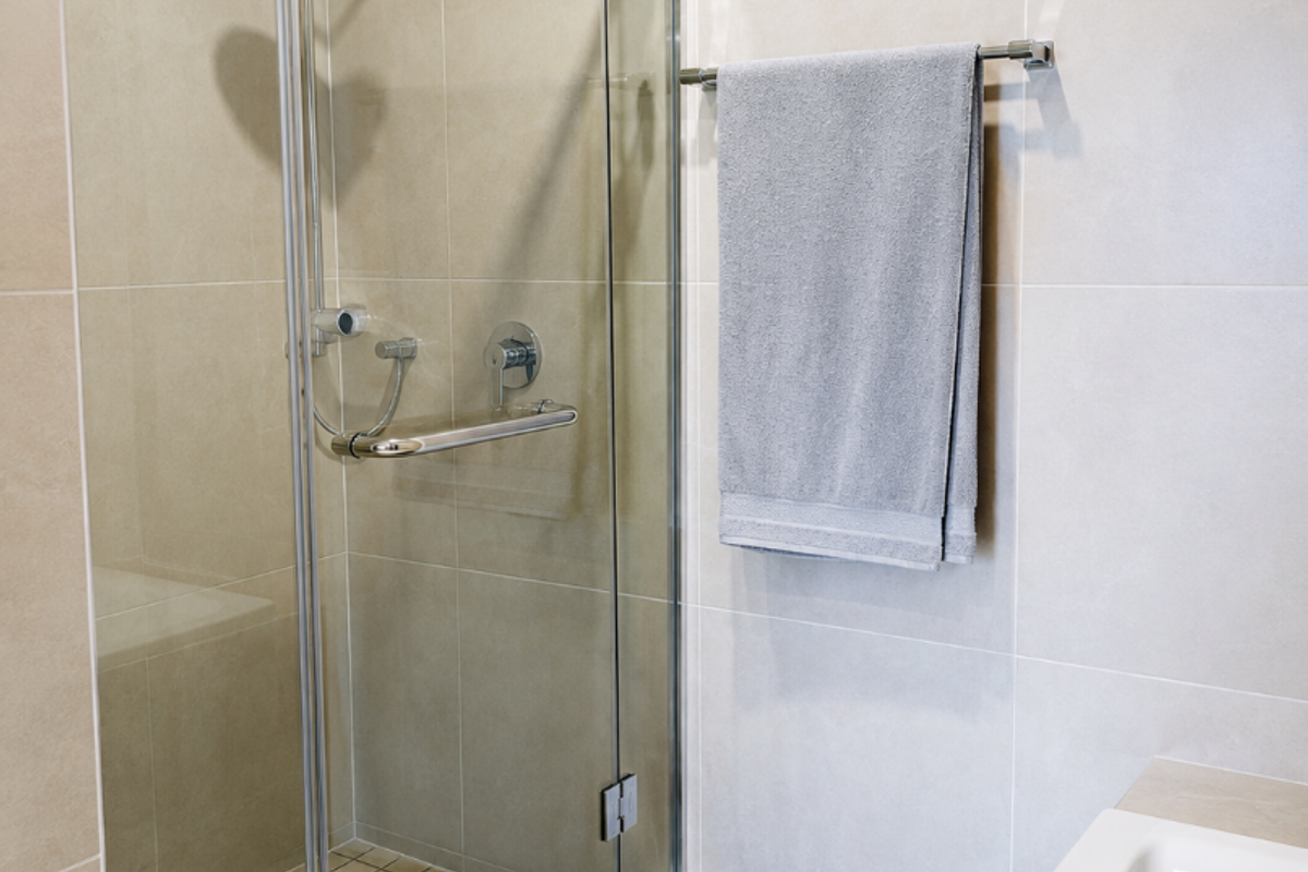 Modern bathroom featuring a glass-enclosed shower with rainfall head, handheld attachment, and a built-in bathtub with neutral ceramic wall tiling.