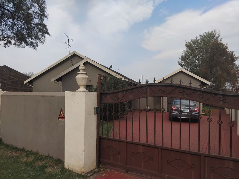 Front view of the property featuring a secure wrought iron gate, perimeter wall, and a paved driveway leading to the house entrance.