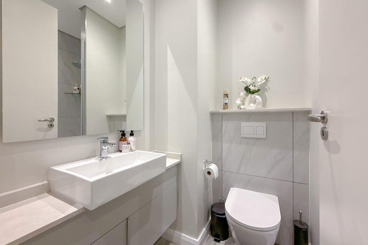 Modern bathroom featuring a wall-mounted toilet, sleek vanity with a vessel sink, large mirror, and neutral marble-look wall tiles.