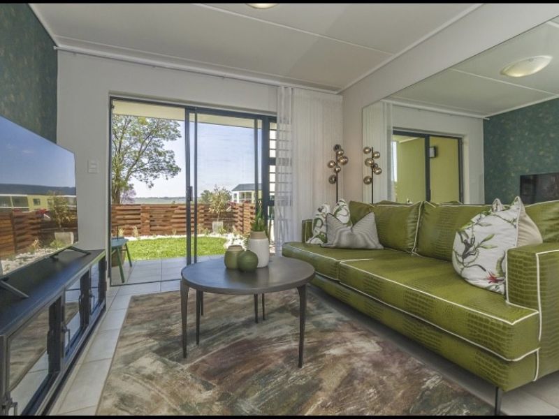 A bright living room featuring tiled flooring, a large wall mirror, and sliding glass doors that open onto a private patio and garden area.