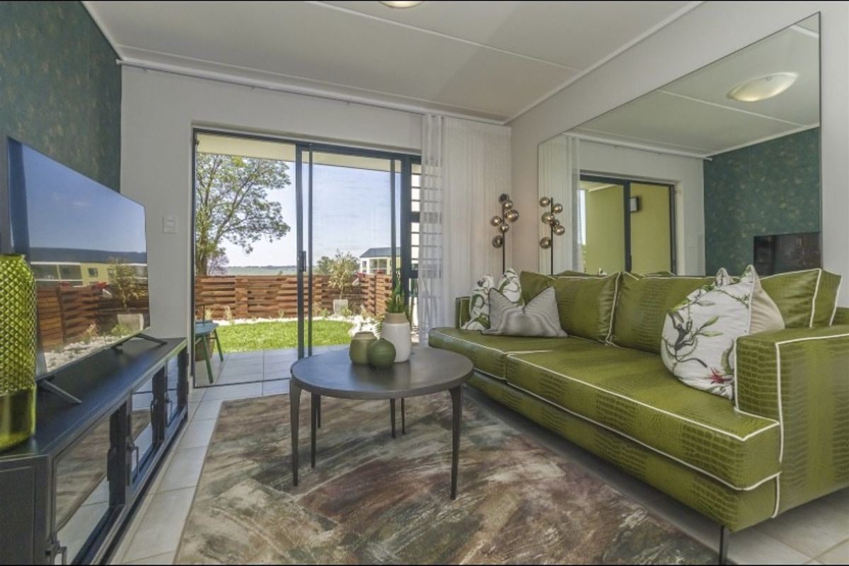 A bright living room featuring tiled flooring, a large wall mirror, and sliding glass doors that open onto a private patio and garden area.