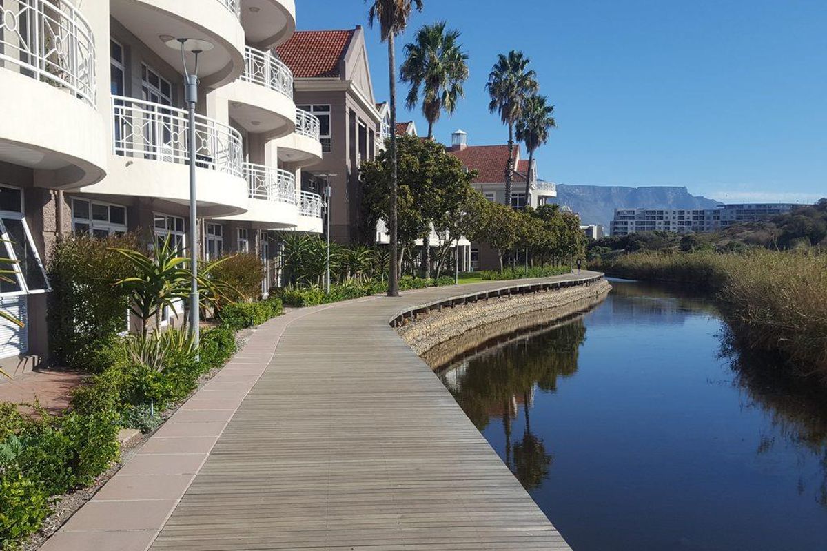 A scenic view of the office complex exterior featuring a wooden boardwalk along a canal with landscaped gardens and mountain views.
