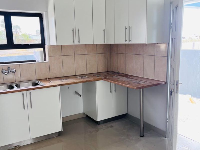 A functional kitchen area featuring white built-in cabinetry, a double sink, tiled backsplash, and a laminate countertop with a breakfast bar extension.