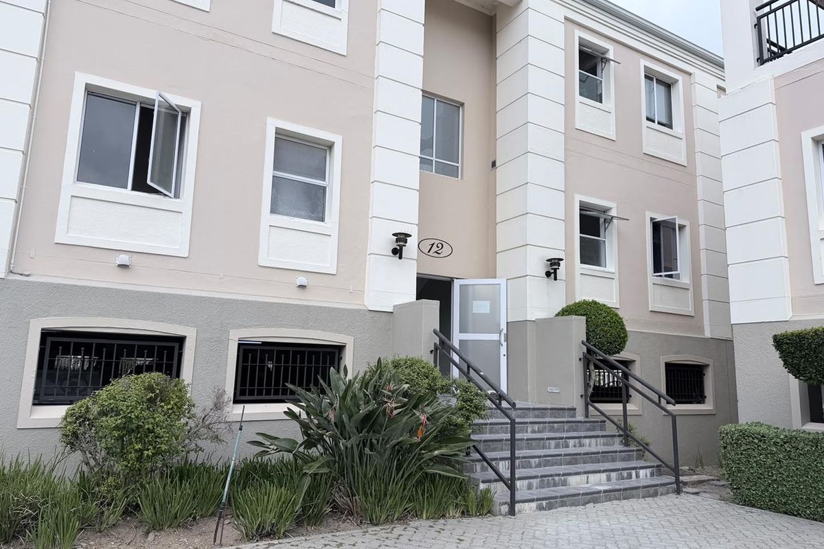 Front elevation of a multi-story office building featuring a paved entrance, tiled staircase with metal handrails, and well-maintained exterior facade.