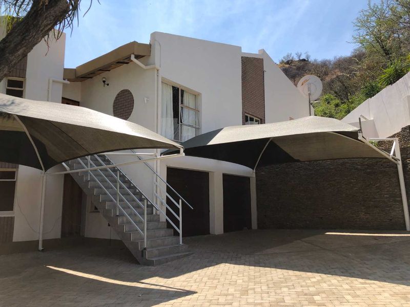 Front exterior view featuring a paved driveway, dual shade sails for parking, and an external staircase leading to the upper level.