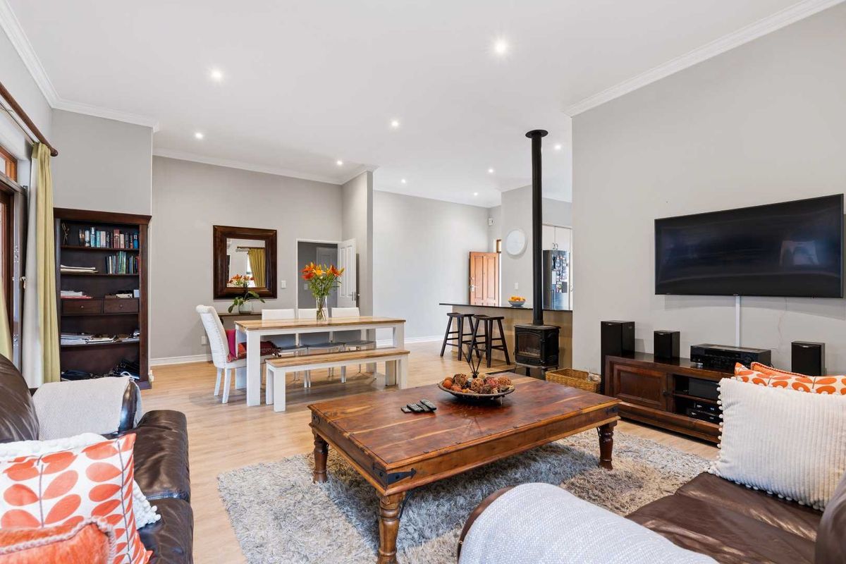 Spacious open-plan living and dining area featuring laminate flooring, recessed lighting, and a central wood-burning fireplace, seamlessly connecting to the kitchen.