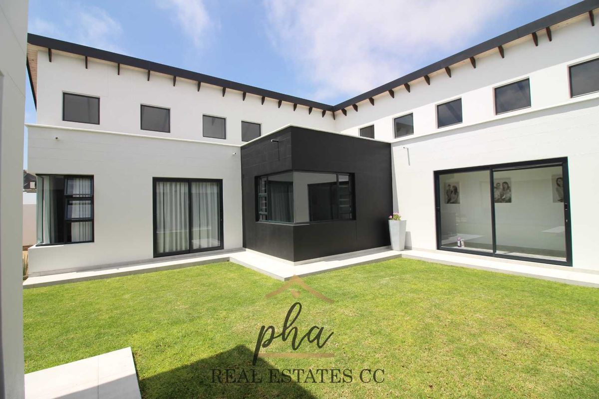 Modern rear exterior view of the house featuring a manicured lawn, clean white facade, and large black-framed sliding glass doors.