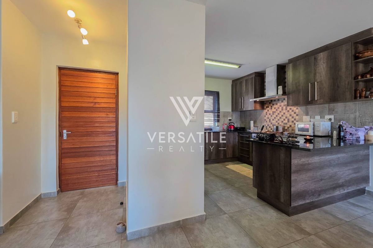 A modern kitchen featuring dark wood cabinetry, granite countertops, a tiled backsplash, and an integrated extractor fan, adjacent to a wooden entry door.