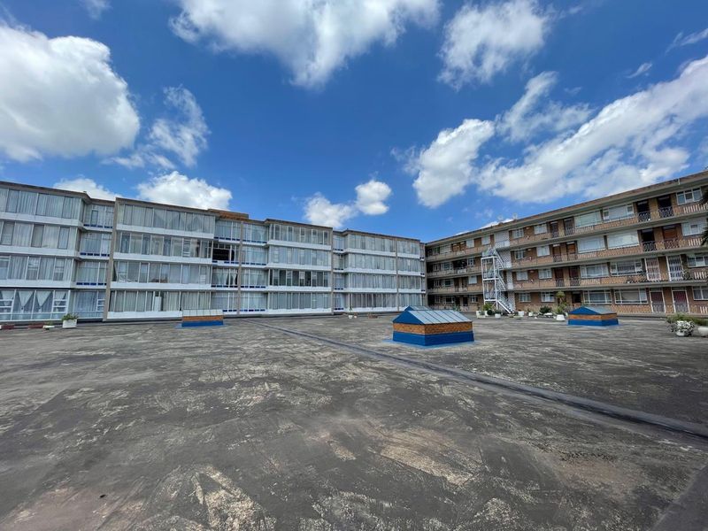 A wide-angle view of a large flat roof area between two multi-story apartment blocks featuring skylights and external stairwell access.