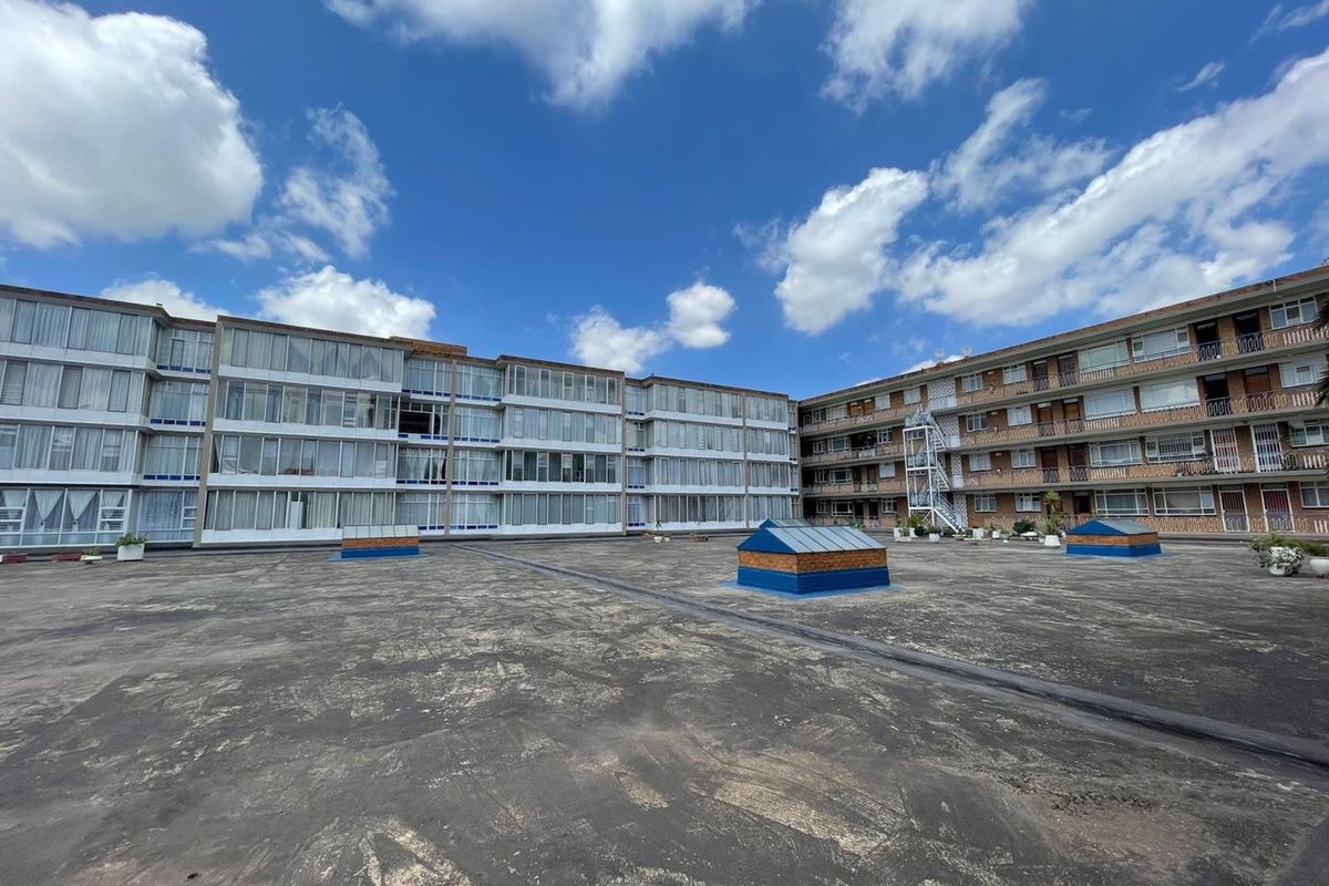 A wide-angle view of a large flat roof area between two multi-story apartment blocks featuring skylights and external stairwell access.