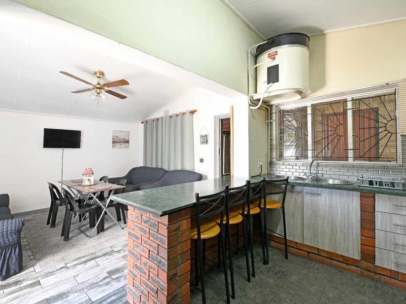 Open-plan living and kitchen area featuring a breakfast bar, brick-based cabinetry, and a ceiling fan, offering a functional layout for daily living.