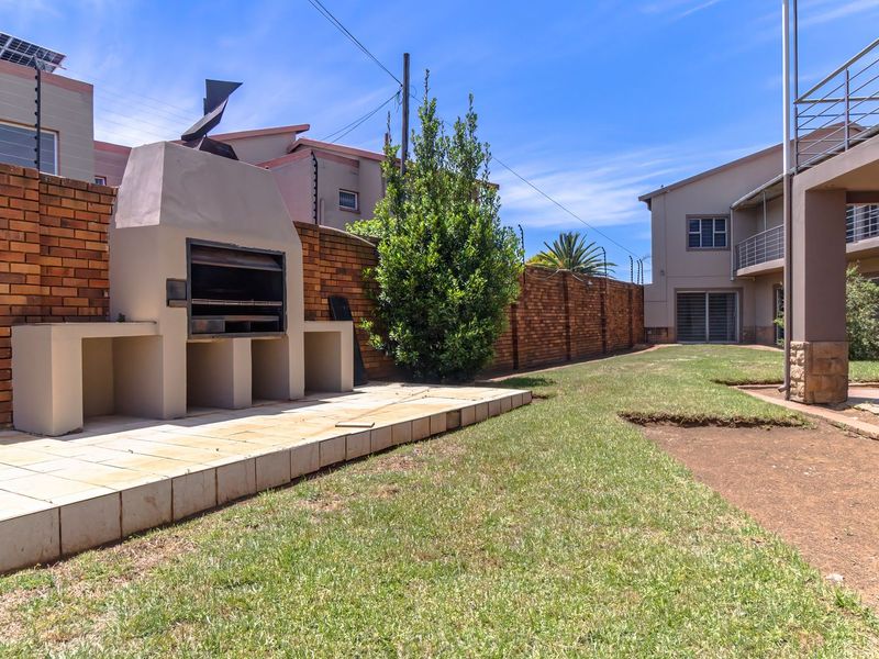 A rear garden area featuring a built-in braai, tiled patio space, and brick boundary walls with electric fencing.