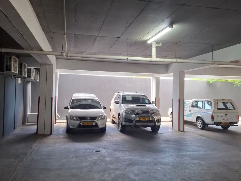 A covered parking garage area featuring concrete flooring, structural columns, and overhead lighting with mounted air conditioning units.