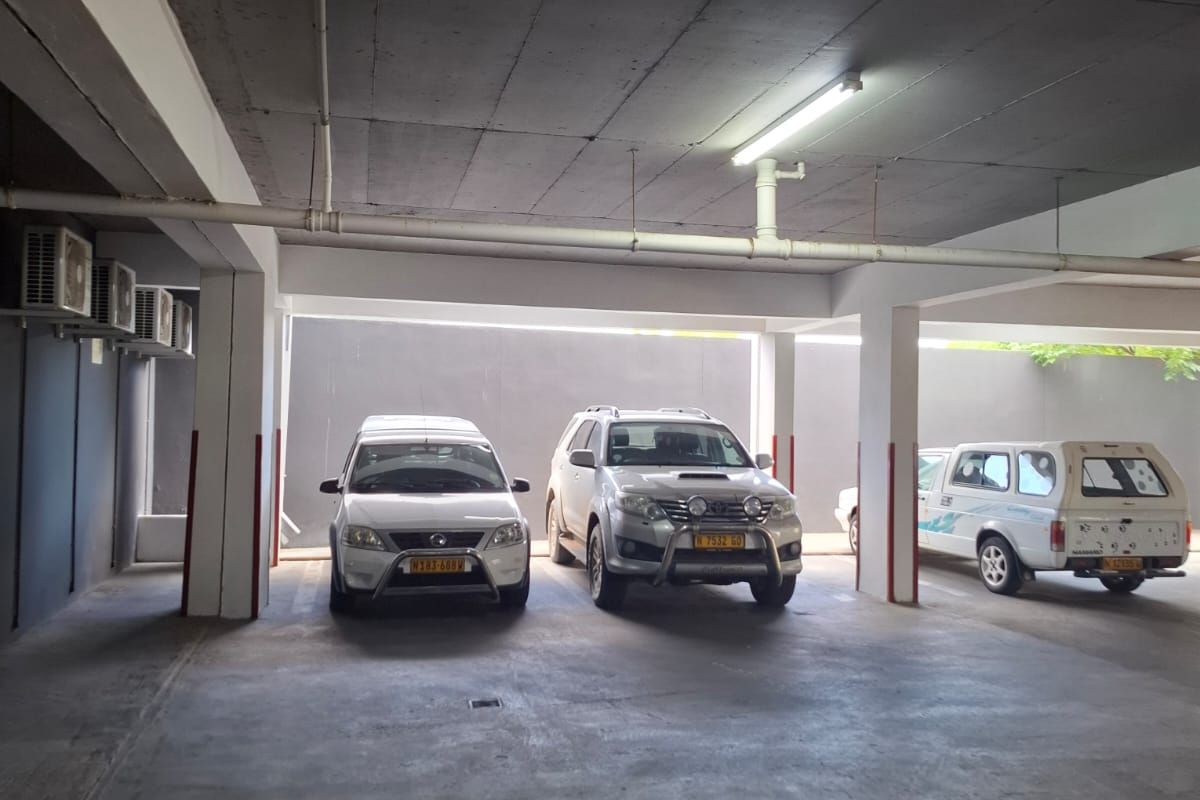 A covered parking garage area featuring concrete flooring, structural columns, and overhead lighting with mounted air conditioning units.