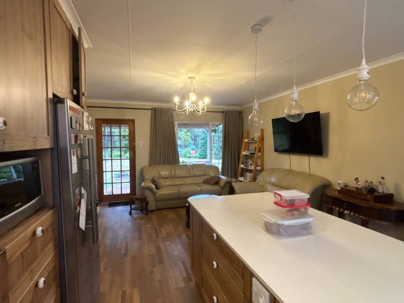 Open plan living and kitchen area featuring timber cabinetry, a central island with stone countertop, and direct access to the rear garden.