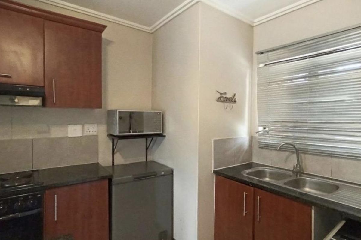 A functional kitchen featuring dark wood-look cabinetry, laminate countertops, a double stainless steel sink, and integrated cooking appliances with tiled splashbacks.