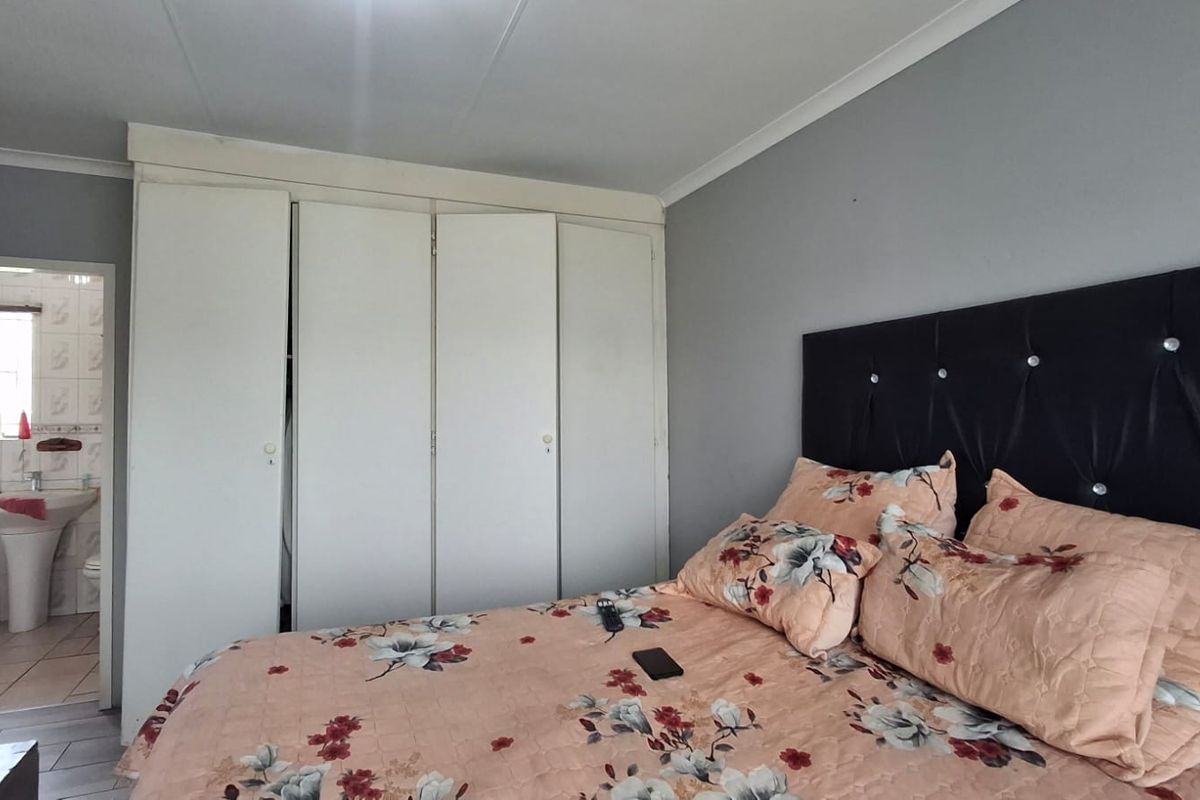 A bedroom featuring built-in cupboards and an adjoining en-suite bathroom with tiled finishes.