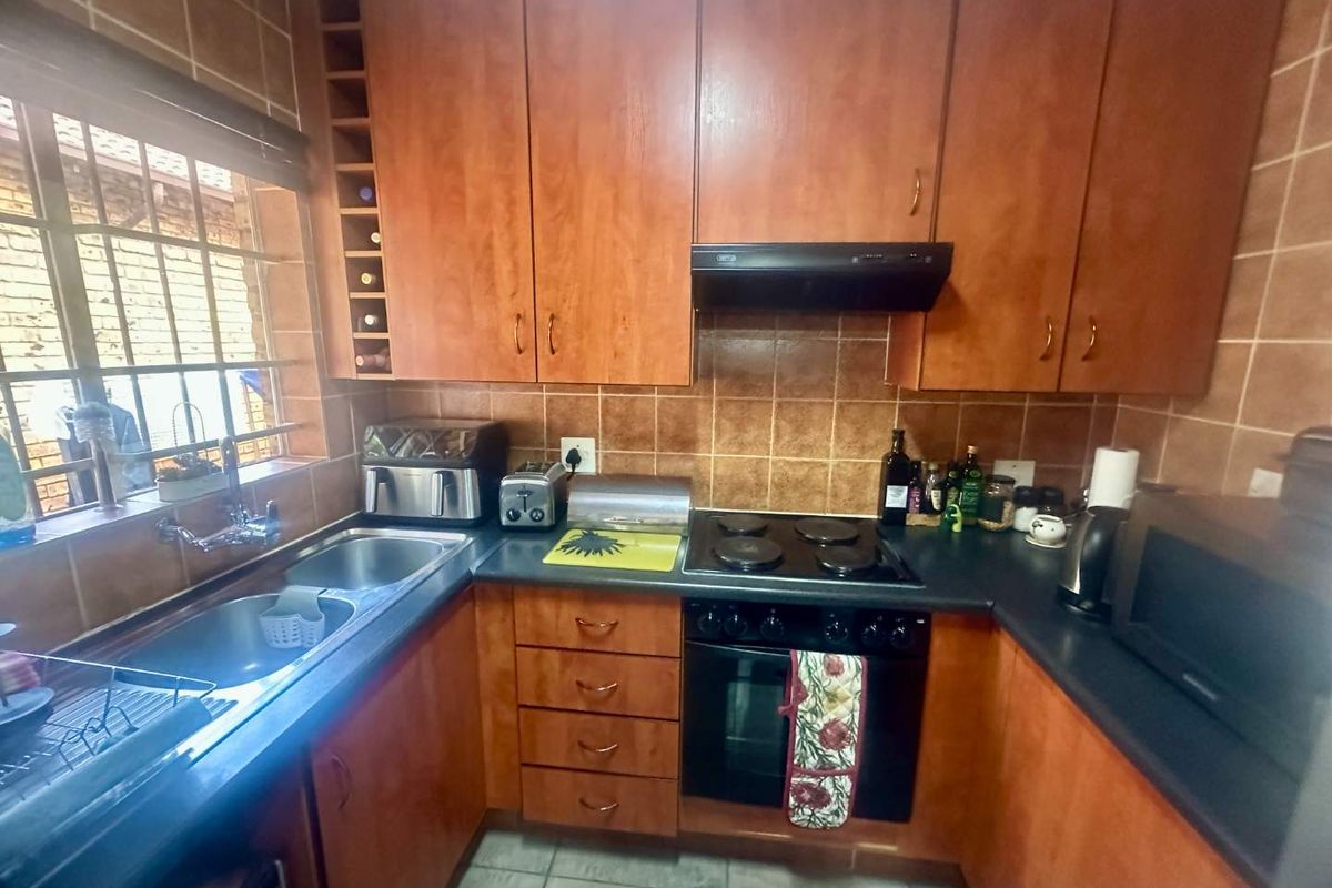A functional kitchen featuring wood-finish cabinetry, dark laminate countertops, a built-in oven with hob, extractor fan, and a double stainless steel sink.