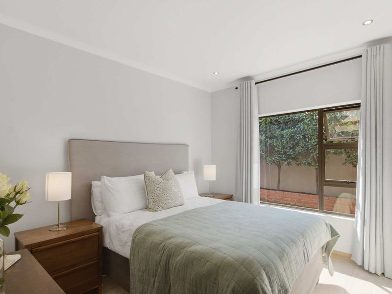 A well-maintained bedroom featuring neutral walls, recessed lighting, and a large window overlooking a private garden area.