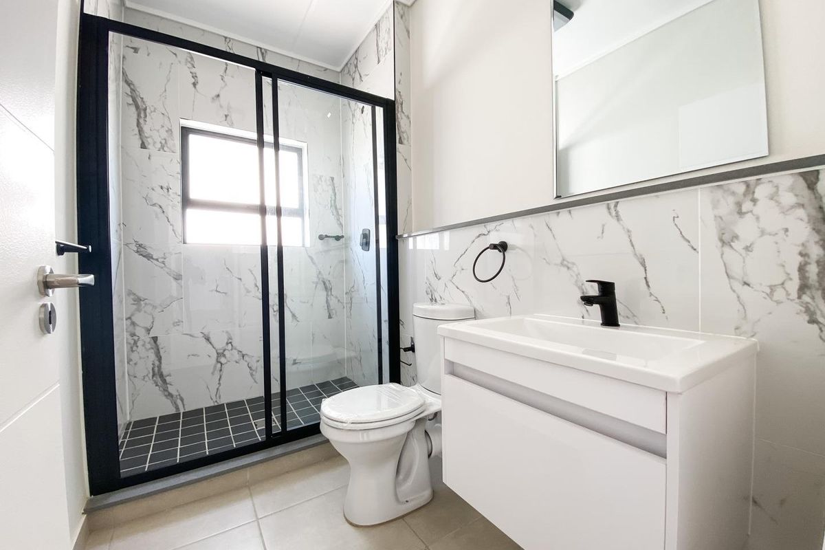 Modern bathroom featuring a walk-in shower with black frame, marble-look wall tiles, vanity unit with black tapware, and a wall-mounted mirror.