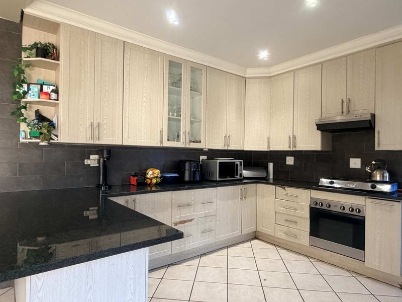 A functional kitchen featuring light wood-grain cabinetry, dark granite countertops, a tiled backsplash, and integrated cooking appliances.
