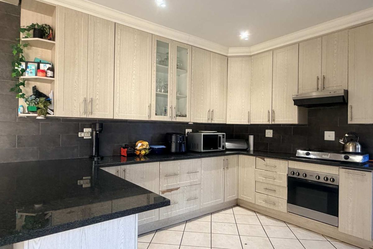 A functional kitchen featuring light wood-grain cabinetry, dark granite countertops, a tiled backsplash, and integrated cooking appliances.