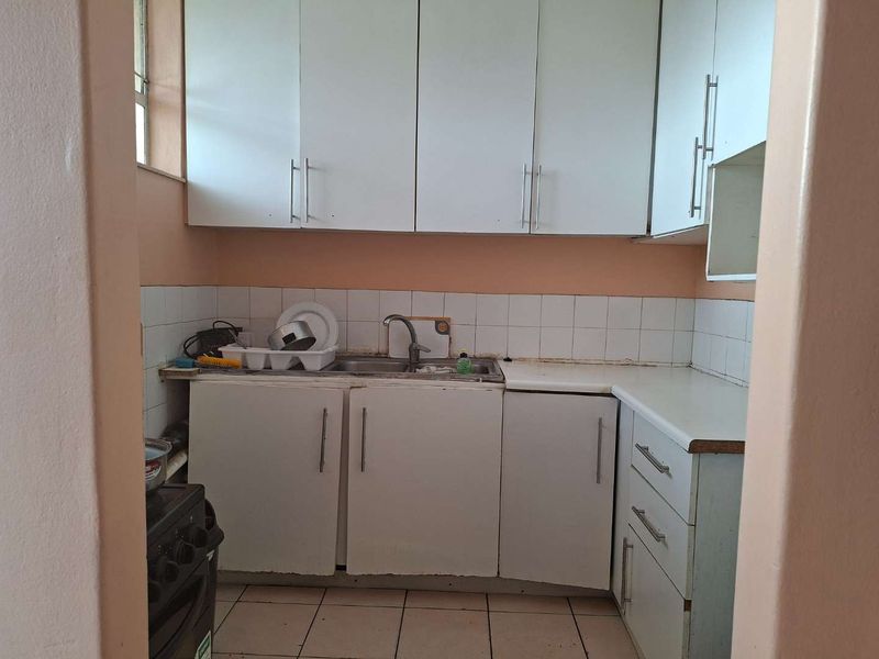 A compact kitchen featuring white built-in cabinetry, tiled backsplash, and tiled flooring, offering a functional layout with potential for modernization.