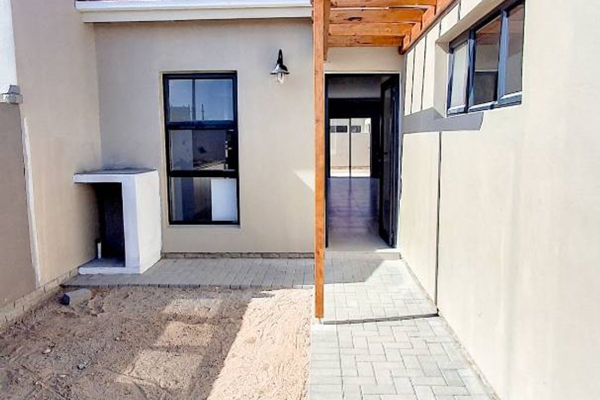 Rear exterior view of the townhouse featuring a paved walkway, timber pergola, and a built-in outdoor counter area.