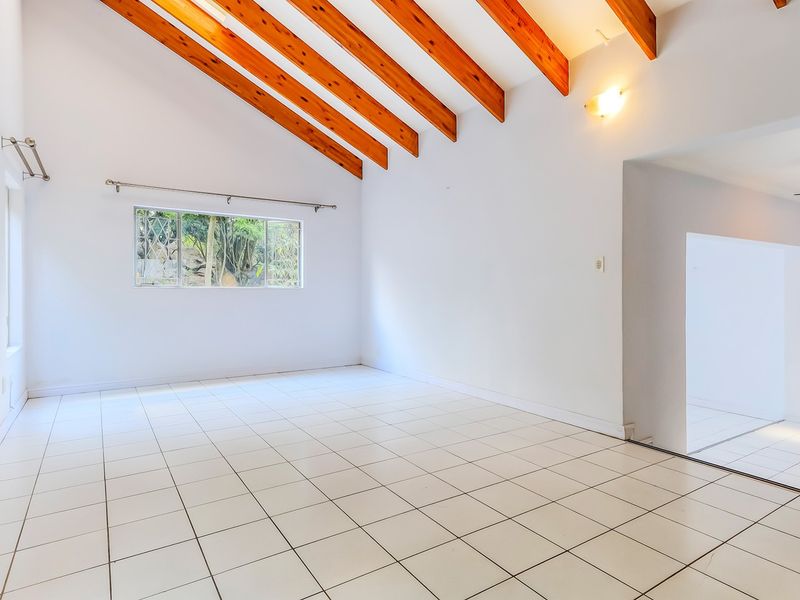Spacious living area featuring a vaulted ceiling with exposed timber beams and neutral ceramic floor tiles, offering a bright and open atmosphere.