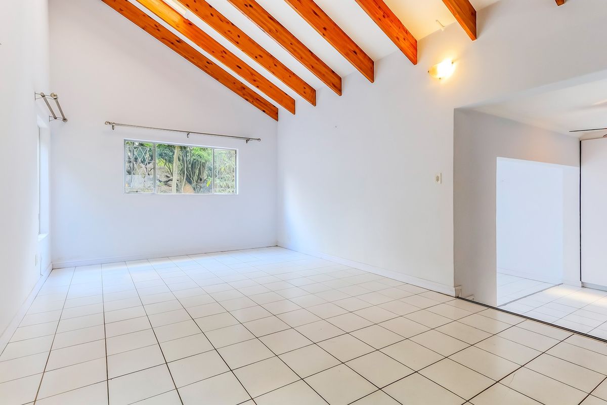 Spacious living area featuring a vaulted ceiling with exposed timber beams and neutral ceramic floor tiles, offering a bright and open atmosphere.